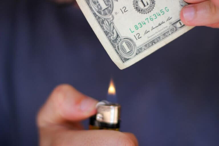 Hands holding a lighter flame to a dollar bill
